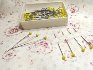 Gule knappenåle i lille æske placeret på blomstret stof.