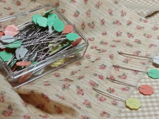 Clover Flower Head Pins i pastelfarver i klar æske, vist på patchworkstof – ideelle til patchwork og quiltning.